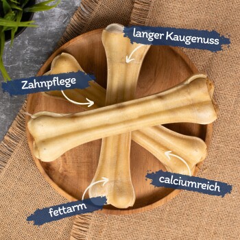 Vier Hundekauknocken auf einem Holzbrett, beschriftet mit Vorteilen: Zahnpflege, langanhaltendes Kauen, fettarm und reich an Kalzium.