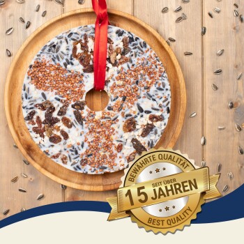 Ein runder Vogelfutterkuchen mit einem roten Band auf einem Holzbrett, umgeben von Sonnenblumenkernen und einem 'Best Quality'-Abzeichen.
