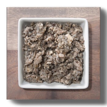 Ein quadratisches weißes Geschirr, gefüllt mit einer stückigen, grauen Tiernahrungsmischung, auf einer Holzoberfläche platziert.