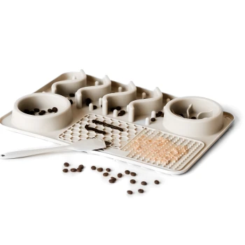 Eine beige Futtermatte für Haustiere mit zwei Schalen, eine spiralförmig gestaltete, texturierte Abschnitte zur Futteranreicherung, verstreute Kroketten und einen Spatel.