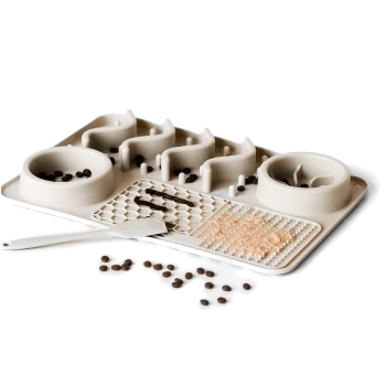 Eine beige Futtermatte für Haustiere mit zwei Schalen, eine spiralförmig gestaltete, texturierte Abschnitte zur Futteranreicherung, verstreute Kroketten und einen Spatel.