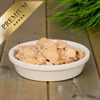 Eine schwarze Schüssel mit zerkleinertem Nassfutter für Katzen steht auf einer strukturierten Oberfläche, umgeben von bunten Spielzeugmäusen und Federn.