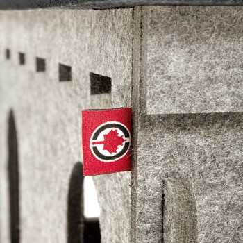 Nahaufnahme eines grauen Filzhaustierhauses mit einem roten Etikett, das ein schwarz-weißes Logo mit einem Ahornblatt zeigt.