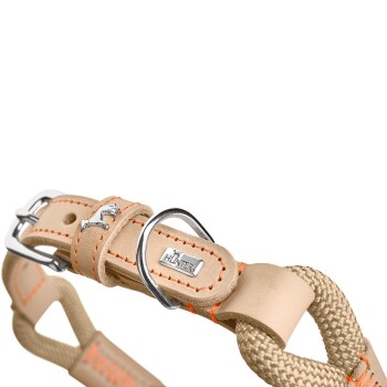 Eine Nahaufnahme eines beigen Hundegeschirrs mit orangefarbenen Nähten, Metall-Schnallen und einem silbernen "HUNTER"-Logo-Anhänger.