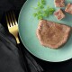 Eine Portion Haustierfutter auf einem türkisfarbenen Teller, begleitet von einem Zweig Petersilie und kleinen Würfeln des gleichen Futters, mit einer goldenen Gabel daneben.