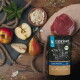 LIEBESGUT Bio-Kitten-Rind-Futterbeutel neben rohem Steak, Äpfeln, Birnen und Kokosraspeln auf einer Holzoberfläche.