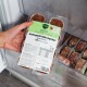 Hand hält eine Packung gefrorener Hundefutter‑Patties mit der Aufschrift 'Komplett‑Mix Senior Rind & Huhn' über einer Gefrierschublade
