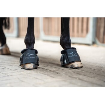 Eine Nahaufnahme der Vorderbeine eines Pferdes, das schwarze Hufschuhe mit dem Logo 'EQUINATE' an den Riemen trägt, auf einer Kopfsteinpflasteroberfläche.