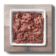 Rohes Haustierfutter in einer weißen quadratischen Schüssel, bestehend aus einer Mischung aus fein gemahlenem Fleisch mit einer reichen roten Farbe, auf einer Holzoberfläche platziert.