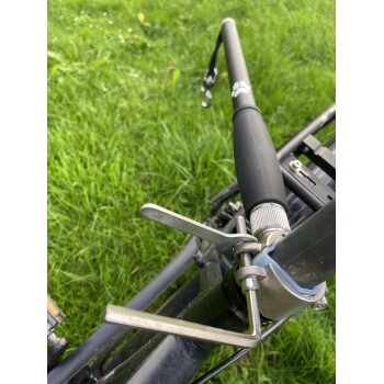 Nahaufnahme einer schwarzen Angelrute, montiert auf einem Metallrutenhalter mit Klemme, vor grünem Gras-Hintergrund.