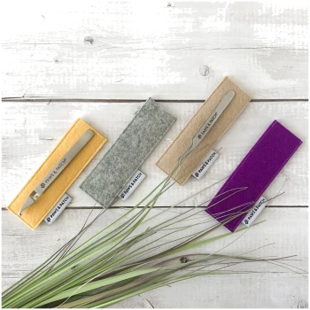 Vier Edelstahlpinzetten auf gelben, grauen, beigen und violetten Filzüberzügen mit der Aufschrift „PAWS & PATCH“ auf weißem Holzuntergrund.