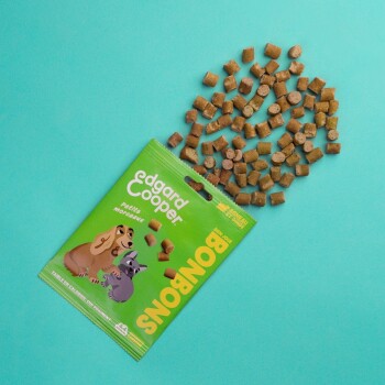 Emballage de friandises pour animaux de compagnie Edgard Cooper Bonbons avec des croquettes éparpillées, mettant en avant des chiens de dessin animé sur un fond vert vif.