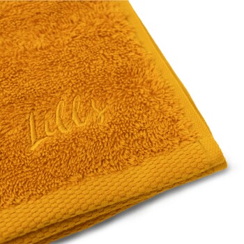 Eine Nahaufnahme eines weichen, leuchtend gelben Handtuchs mit dem gestickten Namen 'Lilly's', das seine plüschige Textur zeigt.