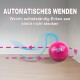 Pinkes Modern CAT-Rollspielzeug mit blauem Schwanz in einem Raum; deutscher Text: AUTOMATISCHES WENDEN und ‚vermeidet Ecken, bleibt nicht stecken‘.