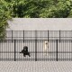 Zwei Hunde, ein schwarzer Labrador und ein gelber Labrador, stehen hinter einem schwarzen Metallzaun in einem Haustiergehege mit Grün im Hintergrund.