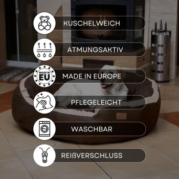 Hund liegt in einem braun-beigen Haustierbett vor einem Kamin mit deutschem Text, der Eigenschaften wie weich, atmungsaktiv, waschbar beschreibt.
