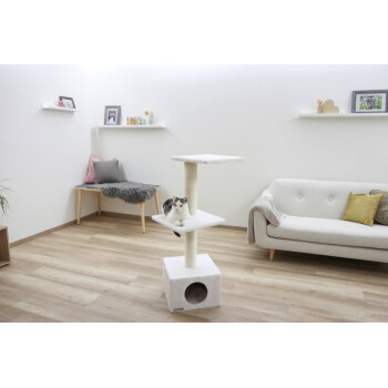 Weiß-graue Katze sitzt auf einem weißen Kratzbaum in einem modernen Wohnzimmer mit grauem Sofa und dekorativen Regalen.