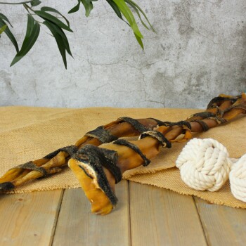 Ein geflochtener Hundekauartikel aus natürlichen Zutaten, auf einer Juteschicht mit einem Holz-Hintergrund platziert, neben zwei weißen Seilspielzeugen.