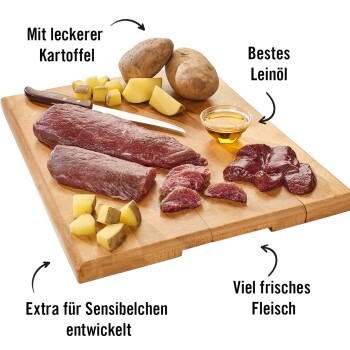 Holzschneidebrett mit frischem Fleisch, gewürfelten Kartoffeln und Öl. Text: "Mit leckerer Kartoffel," "Bestes Leinöl," "Extra für Sensibelchen."