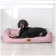 Ein schwarzer Hund mit braunen Abzeichen liegt bequem auf einem rosa Haustierbett mit einem kleinen Kissen, mit einem Holzanhänger, auf dem "tierland" steht.