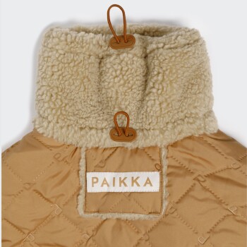 Beiger gesteppter Haustiermantel mit cremefarbenem Sherpa-Kragen, zwei braunen Knebelverschlüssen und weißem Etikett mit der Aufschrift 'PAIKKA'.