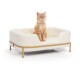 Eine flauschige orange Katze sitzt bequem in einem stilvollen weißen Haustierbett mit einem goldenen Metallrahmen, das ein gemütliches Design zeigt.