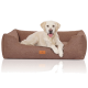 Ein flauschiger weißer Hund liegt auf einem gemütlichen braunen Hundebett mit einem Lederetikett und zeigt Komfort und Stil in einem Tiergeschäft.