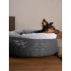 Ein kleiner Hund ruht sich bequem in einem grauen Haustierbett mit einem plüschigen weißen Innenraum aus, mit dem Markennamen "TiaPet" auf der Seite gestickt.