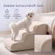 Kleiner weißer Hund auf beige gerippten Haustiertreppen am Bett; deutscher Text ‚Stabiler Schaumstoff-Halt‘ mit Icons.