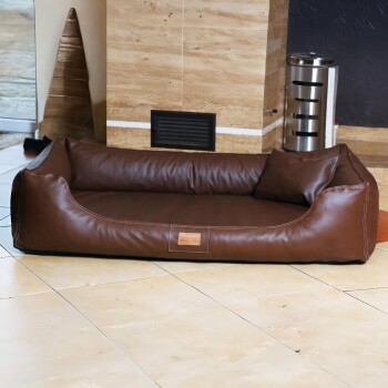 Braunes rechteckiges Haustierbett aus Leder mit gepolsterten Seiten und kleinem Kissen, auf gefliestem Boden im Innenraum.