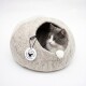Eine Siamkatze mit blauen Augen, die aus einem gemütlichen, grauen Filz-Haustierbett in Form eines Steins schaut, vor einem weißen Hintergrund.