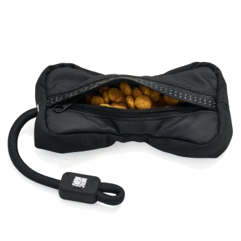 Schwarze, knochenförmige Leckerli-Tasche für Hunde, Reißverschluss geöffnet, runde braune Leckerlis sichtbar, mit Seilschlaufe und schwarzem Etikett mit weißem Logo.