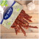 Eine Tüte mit Haustierleckereien mit der Aufschrift "Lyra Nature Power", die Streifen von getrocknetem Fleisch auf einer Holzoberfläche ausgießt, mit einem Seilspielzeug in der Ecke.