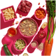 Ein lebendiger pinker Hintergrund zeigt eine große Schüssel mit Hundefutter mit gewürfeltem Fleisch, Karotten, Zucchini, Apfel, einem Glas Flüssigkeit und Trockenfutterstücken.