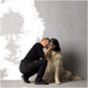 Eine Frau in schwarzer Kleidung kniet neben einem großen, flauschigen Hund und berührt sanft sein Gesicht, was eine liebevolle Bindung zeigt.