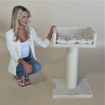 Eine Frau in einem weißen Blazer kniet neben einem plüschigen Katzenbaum mit einem weichen, gepolsterten Bett oben und einem strukturierten Kratzbaum.