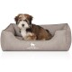 Ein kleiner, flauschiger Hund sitzt bequem in einem grauen Hundebett, auf dessen Vorderseite das Logo "KNUFFELWUFF" deutlich zu sehen ist.