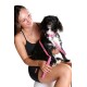 Eine Frau in einem schwarzen Tanktop und Shorts hält einen kleinen schwarz-weißen Hund mit einem rosa Geschirr und Leine, vor einem weißen Hintergrund.