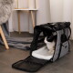 Dreifarbige Katze sitzt in einer geöffneten grauen, weichen Transporttasche mit weißer Plüschauflage auf dem Boden, im Hintergrund Stuhl und Decke.