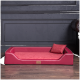 Rotes Hundebett mit einem plüschigen Kissen und einem kleinen passenden Kissen, vor einer dunklen Wand und einem Holzboden.