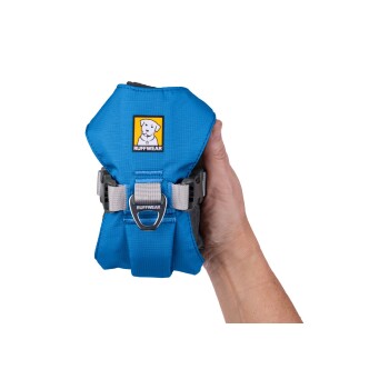 Eine Hand hält ein blaues Hundegeschirr mit einem Ruffwear-Logo, mit verstellbaren Riemen und einem Metallbefestigungspunkt.