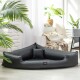Ein schwarzes dreieckiges Haustierbett mit einem kleinen Kissen, in einem hellen Raum mit Pflanzen und weichen Möbeln im Hintergrund.