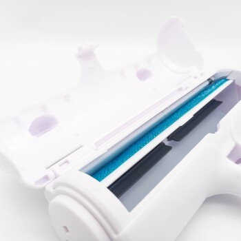 Eine Nahaufnahme eines weißen Werkzeugs zur Entfernung von Haustierhaaren mit einem blauen Reinigungstreifen und einem Fach zur Sammlung von Haaren, teilweise geöffnet.