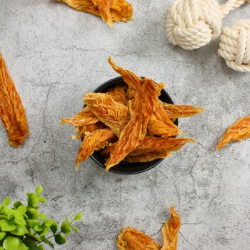 Eine schwarze Schüssel gefüllt mit knusprigen, goldbraunen Hähnchenstreifen, umgeben von verstreuten Stücken desselben Leckerli und einer kleinen grünen Pflanze.