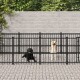 Zwei Hunde, ein schwarzer Labrador und ein gelber Labrador, befinden sich in einem schwarzen Metallhundezwinger mit einer Steinmauer und Grün im Hintergrund.