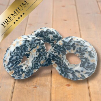 Drei Premium-Vogelfutter-Donuts mit einer weißen Basis und einer Füllung aus schwarzen Sonnenblumenkernen, auf einer Holzoberfläche präsentiert.