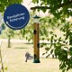 Ein Vogelhaus, das von einem Baum hängt, gefüllt mit Samen, mit einem kleinen Vogel, der sich ihm nähert. Textüberlagerung lautet "Ganzjahresfütterung."