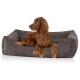 Ein brauner Irish Setter Hund, der in einem gemütlichen, grauen Cord-Haustierbett mit einem Lederetikett entspannt und aufmerksam zur Seite schaut.
