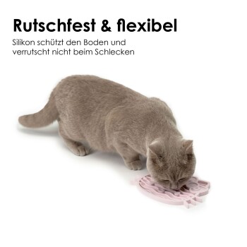 Eine hellgraue Katze leckt eine rosa, uhu-förmige Silikonmatte mit der Aufschrift "Rutschfest & flexibel", die ihre rutschfesten Eigenschaften hervorhebt.