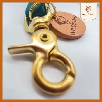 Nahaufnahme eines goldenen Metallclips, der an einem türkisfarbenen Riemen befestigt ist, mit einem runden Lederetikett, das "WILDFANG" mit einem Wolf-Logo zeigt.